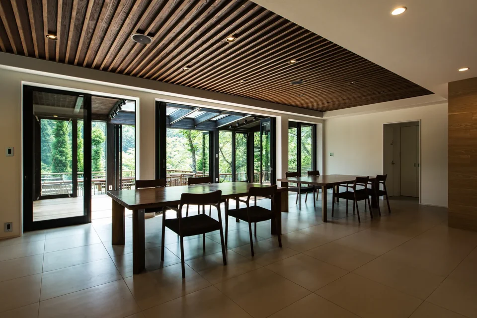 亀岡のVILLA／保養所リノベーション1。木の格子天井のダイニングから、ガラス張りの空間越しに庭の緑を望む